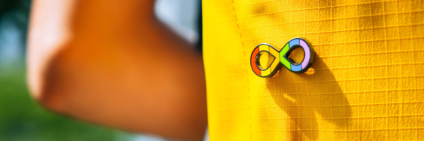A rainbow infinity symbol pin on a yellow backpack