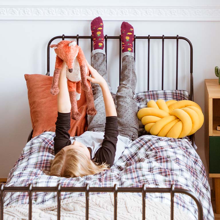 A girl laying in bed with her feet up and holding a stuffed animal