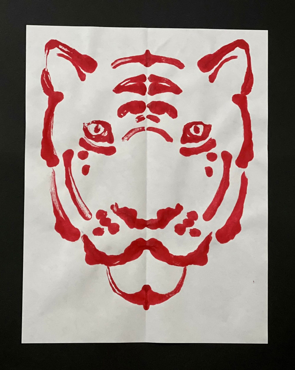 A painting of a tiger in red on a white piece of paper.